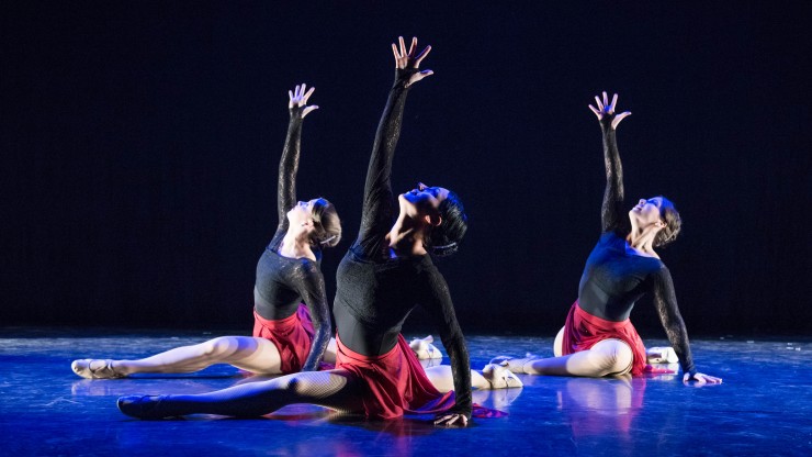 Three students on the floor onstage with their hand stretched up during a dance performance. 