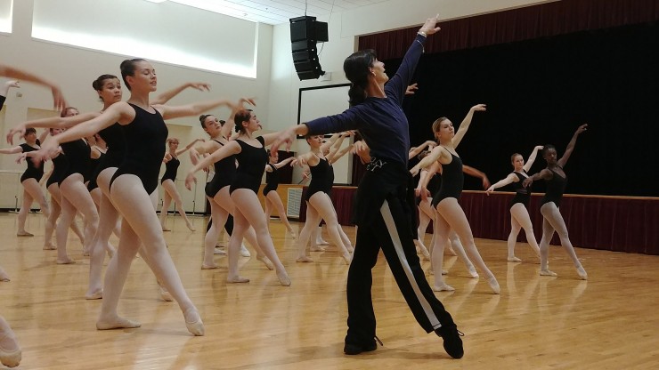 A dance professor leading students through dance during class while the group follows along. 