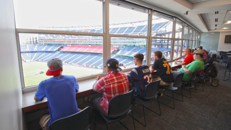 Students receiving a tour of Gillette Stadium sit overlooking the field.