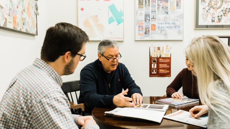 A professor sits with three students to explain the business programs. 