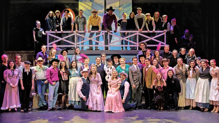The entire cast of a theatre performance smiling while in costume onstage.