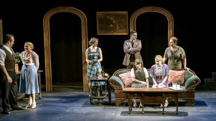 Students are gathered in a living room during a theatre performance.