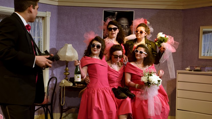 Five students wearing sunglasses looking at another student during a scene from a theatre performance.
