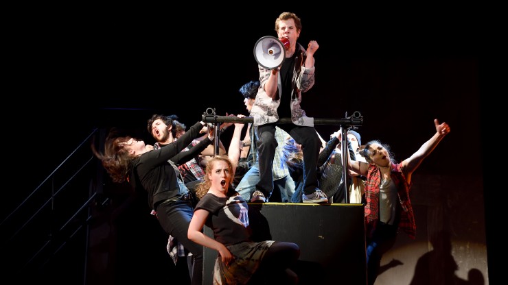 Students singing while hanging off a platform during the American Idiot performance.
