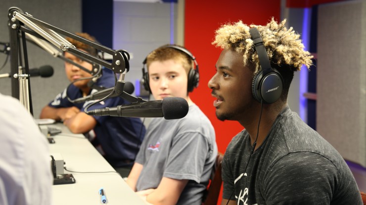 Students in the radio station at Gillette Stadium talking into the broadcasting microphones. 