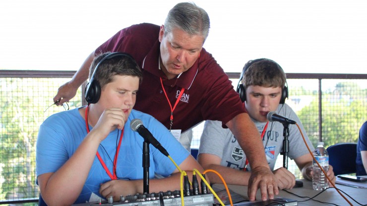 A professor helps students adjusting the soundboard while they are gaining hands-on experience as radio broadcasters.