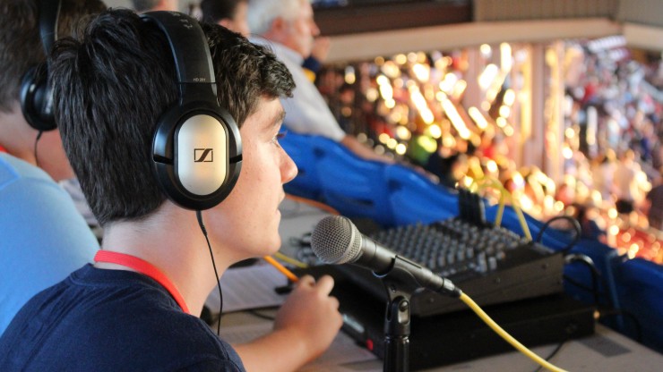 A student wearing headphones sits in front of a microphone while gaining experience as a sports broadcaster at McCoy Stadium during a Pawtucket Red Sox game.