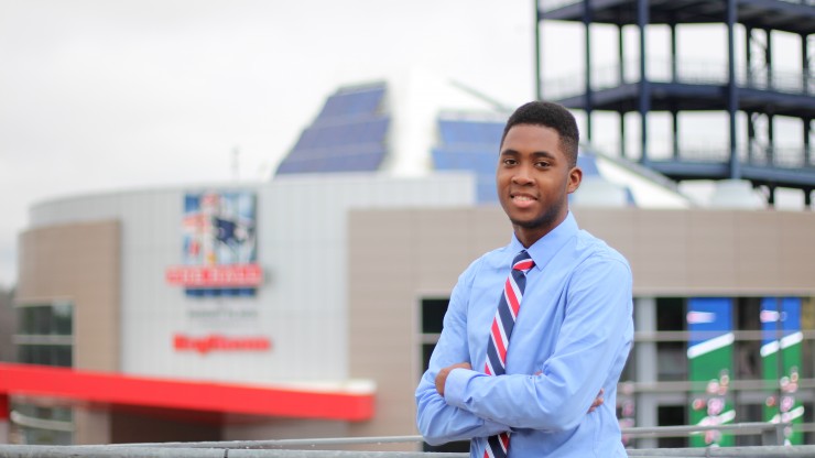 A student stands proudly smiling in front of Gillette Stadium. 