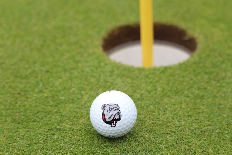image of a golf ball with the dean college bulldog logo that is on putting green next to the hole at the President's Cup Golf Tournament